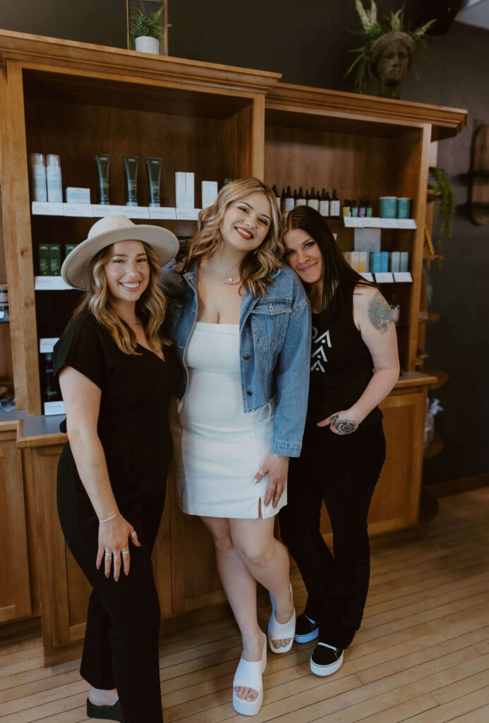 - Ibi David Salon in Westlake, OH Three women pose and smile in front of wooden shelves with beauty products in a modern salon or spa setting. - Ibi David Salon in Westlake, OH