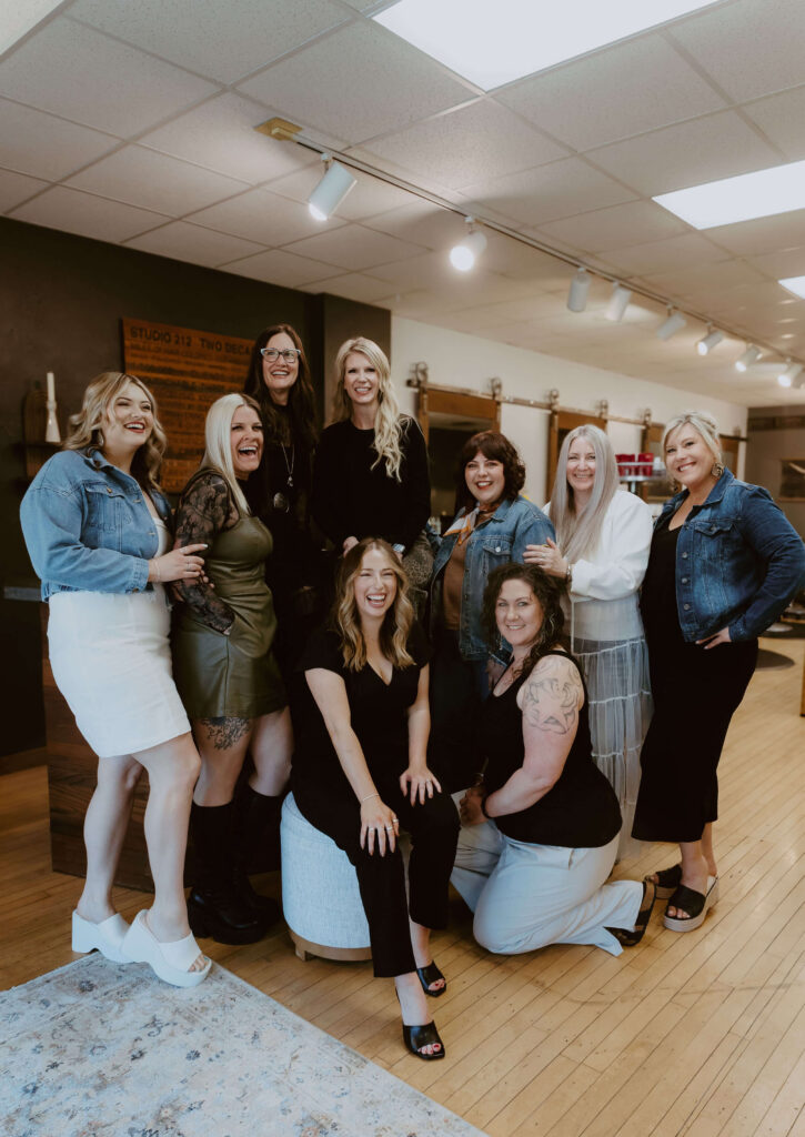 - Ibi David Salon in Westlake, OH A group of nine women pose together indoors, dressed in a mix of casual and semi-formal outfits, smiling at the camera in a well-lit room with wooden floors. - Ibi David Salon in Westlake, OH