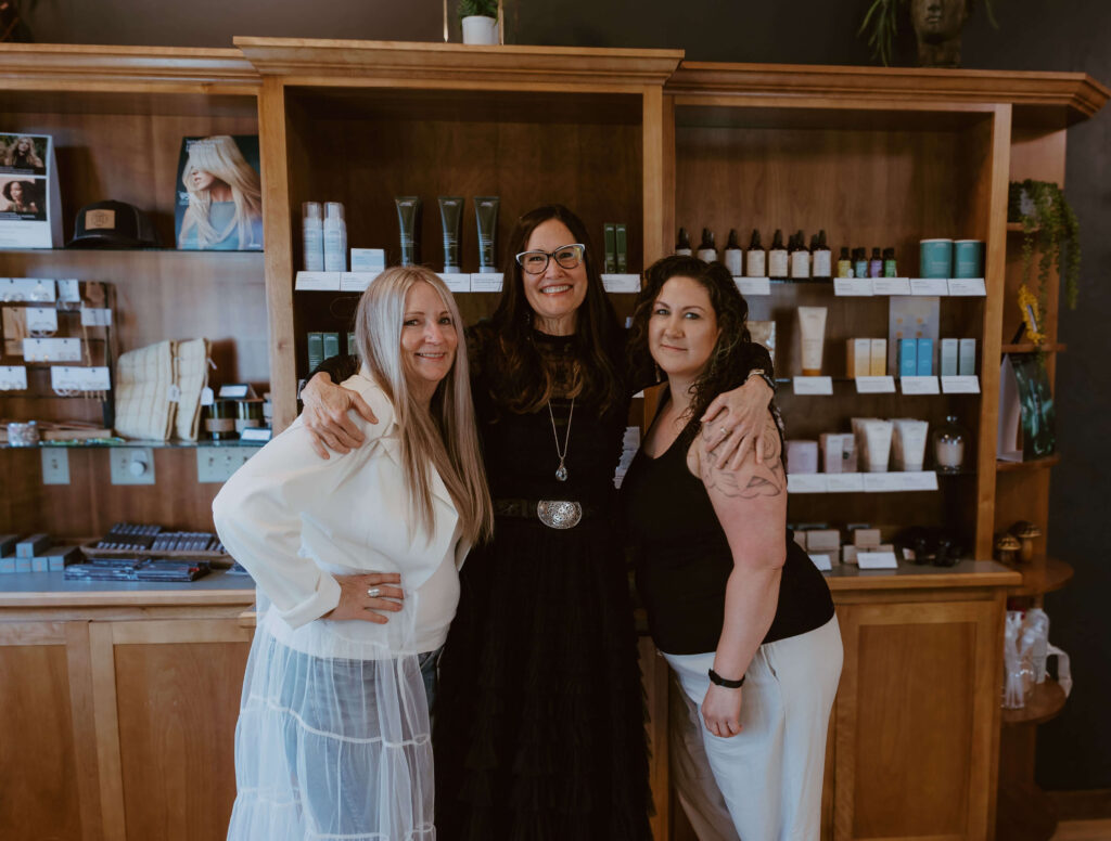 - Ibi David Salon in Westlake, OH Three women standing together, smiling, in front of wooden shelves displaying various beauty and skincare products. - Ibi David Salon in Westlake, OH