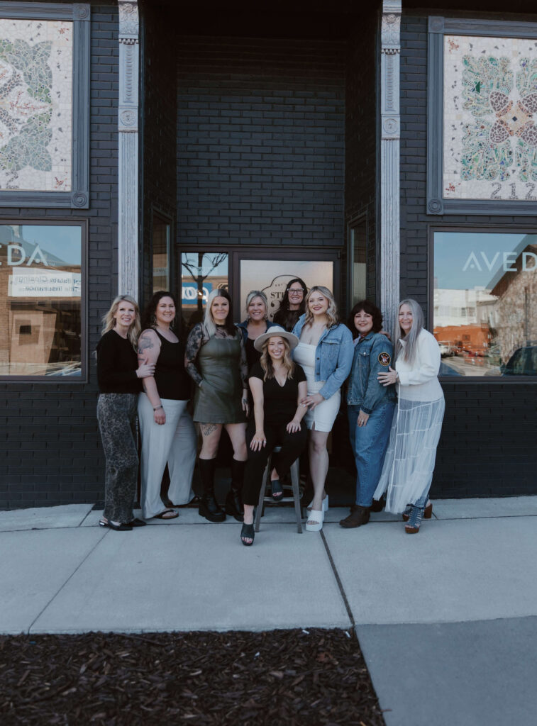 - Ibi David Salon in Westlake, OH Nine women pose together outside a salon with black brick walls and decorative panels. Most are standing, one is seated on a stool, and all are facing the camera. - Ibi David Salon in Westlake, OH